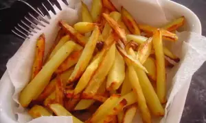 Un plat blanc rempli de délicieuses frites au four, dorées et croustillantes, prêtes à être dégustées. Une fourchette est posée sur le bord.