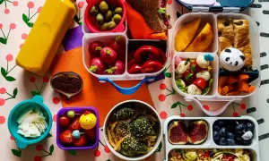 Kolorowy lunchbox z owocami, warzywami, kanapką i napojem.