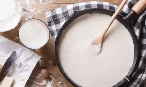 Gładki sos beszamel w patelni, obok mleko, masło i mąka.