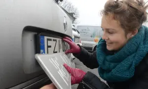Kobieta w czerwonych rękawiczkach mocuje tablicę rejestracyjną do samochodu.