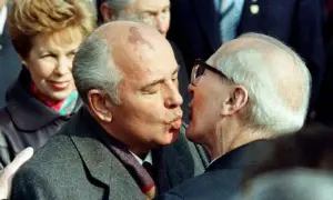 Gorbatschow und Honecker im Bruderkuss. Eine Frau im Hintergrund lächelt.