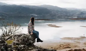 Frau sitzt auf Felsen mit Blick auf einen See und Berge. Ein perfekter Moment während eines Montenegro Roadtrips.
