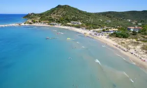 Słoneczny dzień na plaży Alykanas. Turkusowa woda, piaszczysty brzeg z leżakami i parasolami, zielone wzgórza w tle.