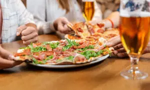 Un gruppo di amici condivide una deliziosa pizza con prosciutto e rucola, accompagnata da una fresca birra.