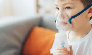 Chłopiec w masce inhalatora z niebieską opaską, wykonujący inhalację.