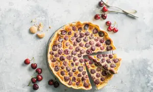 Tarte aux cerises à l'ancienne, garnie de fruits rouges juteux et saupoudrée de sucre glace. Une part est déjà servie.