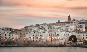 Vieste lungomare al tramonto, con case bianche aggrappate alla collina e il mare calmo.