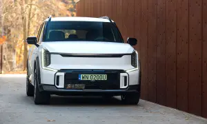 Biały Kia EV9 z polskimi tablicami WN 0200U zaparkowany przy drewnianym ogrodzeniu, jesienne liście na ziemi.
