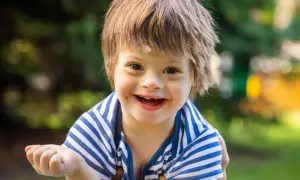 Un bambino sorridente con la sindrome di Down, con i suoi tratti distintivi, indossa una maglietta a righe blu e bianche.