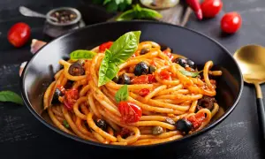Un plat de pâtes aux anchois, tomates, olives et câpres, garni de basilic frais. Un délice méditerranéen.