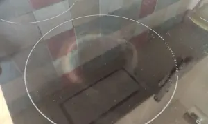 Przegrzana płyta indukcyjna z widocznymi plamami i zarysowaniami. Widać odbicie kafelków i fragmenty okapu.