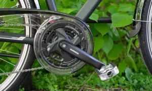 Część napędu roweru trekkingowego Shimano z korbą i zębatkami. Gotowy do jazdy po zielonym tle.