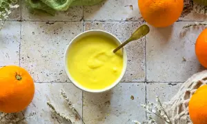 Crema gialla e liscia in una ciotola, con arance fresche intorno. Un cucchiaio dorato è immerso nella crema, che ricorda il sapore del sale all'arancia.