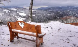 Drewniana ławka z wyciętym sercem i napisem "miasto Wisła" na tle zimowego krajobrazu. Widok na ośnieżone wzgórza i dolinę.