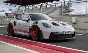 Biały Porsche 992 GT3 RS z czerwonymi akcentami i felgami pędzi po torze wyścigowym.