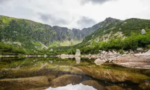 Spokojne, górskie jezioro odbija skaliste zbocza i chmury. To widok z najkrótsza trasa do Śnieżnych Stawków.