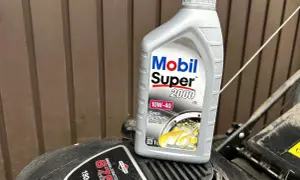 Butelka oleju Mobil Super 2000 10W-40 na silniku kosiarki Briggs & Stratton.