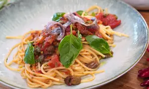 Spaghetti Puttanesca mit Sardellen, Oliven, Kapern und frischem Basilikum auf einem Teller.