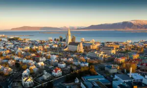 Fakta om Island: Reykjaviks ikoniska kyrka Hallgrímskirkja reser sig över staden med havet och snöklädda berg i bakgrunden.
