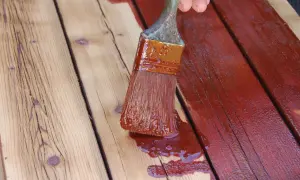Application d'une couche de peinture rouge sur des planches de bois, comme pour repeindre des volets en bois.