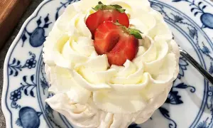 En liten pavlova med fluffig grädde och färska jordgubbar på en vacker blåvit tallrik. En perfekt liten dessert!