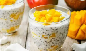 Pyszny deser chia z mlekiem kokosowym i kawałkami mango, podany w szklance. Obok świeże mango i wiórki kokosowe.