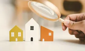 Lente d'ingrandimento esamina tre casette di legno, evidenziando la differenza tra cessione e subentro nel mercato immobiliare.