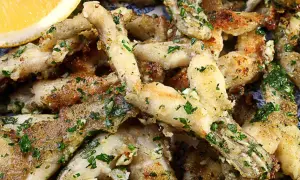 Un plat de cuisse de grenouille frite, garni de persil frais et d'ail, servi avec un quartier de citron.
