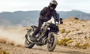 Motocyklista w kasku i kurtce pędzi na motocyklu Honda CB500X po piaszczystej drodze, wzbijając tumany kurzu.