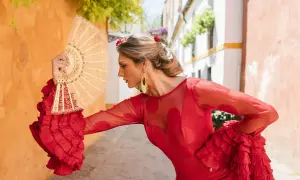 Mujer con peinado de flamenca pelo rizado, vestido rojo volantes, abanico de encaje.