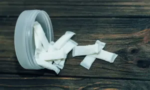 Białe woreczki z nikotyną, popularne jako snus zęby, rozsypane obok plastikowego pojemnika na drewnianym tle.