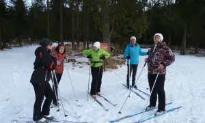 Grupa osób w strojach na narty biegowe pozuje do zdjęcia w zimowym lesie.
