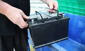 Händer placerar ett bilbatteri i en blå behållare. Kanske för återvinning eller för att byta ut dubbla batterier i bilen.