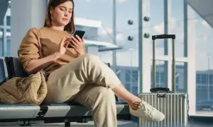 Junge Frau mit Handy in der Airport Lounge, Koffer daneben.