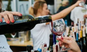 Rödvin hälls upp i ett glas, perfekt vin till lutfisk. Bakgrunden visar en festlig sammankomst med fler vinflaskor.