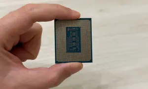 Un dedo sostiene un procesador o CPU, mostrando su parte inferior con pines dorados y un diseño rectangular en el centro.