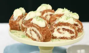 En läcker rulltårta morotskaka med krämig fyllning och lime zest, upplagd på ett gult tårtfat.