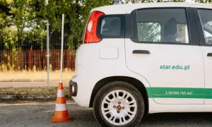 Biały samochód szkoleniowy z pomarańczowym pachołkiem obok. Zastanawiasz się, ile kosztuje prawo jazdy AM? Sprawdź ofertę na star.edu.pl.