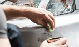Main d'homme nettoyant des éraflures sur un pare-choc plastique, étape de la réparation pare choc plastique.