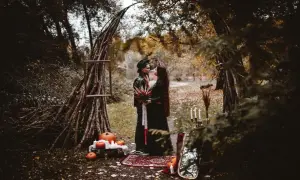 Para w czarnych strojach pod łukiem z gałęzi, dynie i świece.