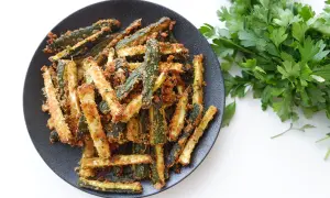 Zucchine gratinate in padella, dorate e croccanti, servite su un piatto nero con prezzemolo fresco.