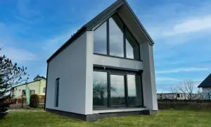 Nowoczesna dobudówka do starego domu, z dużymi oknami i skośnym dachem. Projekty takich budynków to świetny sposób na powiększenie przestrzeni.