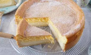 Saftige eierschecke ohne boden, mit Puderzucker bestäubt, auf einem Tortenteller. Ein Stück wurde bereits herausgeschnitten.
