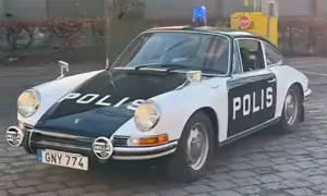 En klassisk Porsche polisbil med blåljus på taket. Bilen är vit med svarta detaljer och texten "POLIS" på motorhuven och dörren.