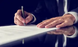 Mężczyzna w garniturze podpisuje dokument. Dowiedz się, jak uzyskać odpis aktu zgonu, aby dopełnić formalności.