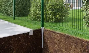 Montaż słupków ogrodzeniowych instrukcja: zielony słupek z metalową stopą wbity w ziemię, obok betonowy chodnik i siatka ogrodzeniowa.