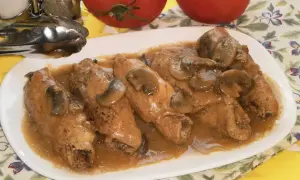 Pyszne gołąbki z pieczarkami w sosie, podane na białym talerzu. Obok stoją pomidory i przyprawniki.