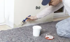 Maler streicht mit Pinsel über Wasserflecken an der Wand, um sie zu überdecken.
