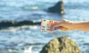 Dłoń trzyma banknoty euro na tle morza. Czarnogóra walutą i językiem jest w Europie.