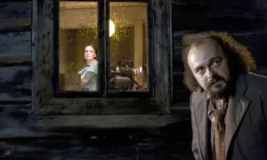 Mężczyzna z kręconymi włosami patrzy w stronę okna, w którym stoi kobieta. Scena z filmu "Dom zły", obsada aktorska.
